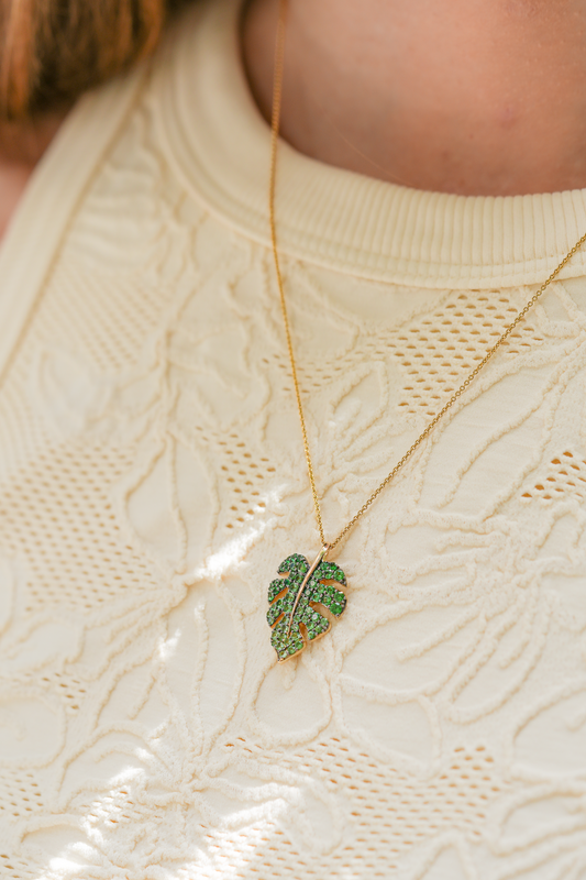 Close up of a model wearing a yellow gold Monstera pendant green tsavorite on a chain. Item No. 772248