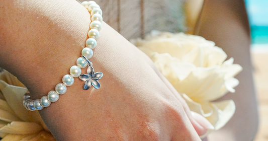 Close-up of a wrist wearing a white pearl bracelet with a silver plumeria charm.