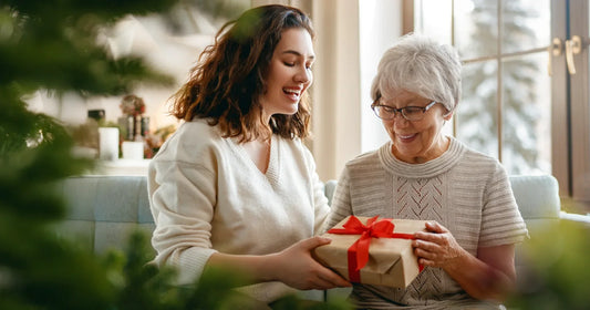 Adult daughter giving a gift to older mom in a cozy indoor setting.