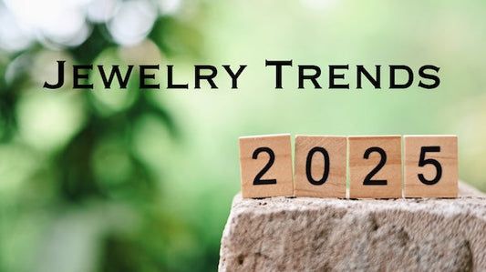Text: "Jewelry Trends", 2025 written on wooden blocks sitting on a rock, blurry tree leaves in background