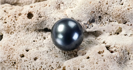 Close up of a single Tahitian "black" pearl on a tan rock.