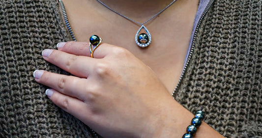 Close-up of a hand across the upper chest wearing a Tahitian pearl ring, bracelet and  pendant