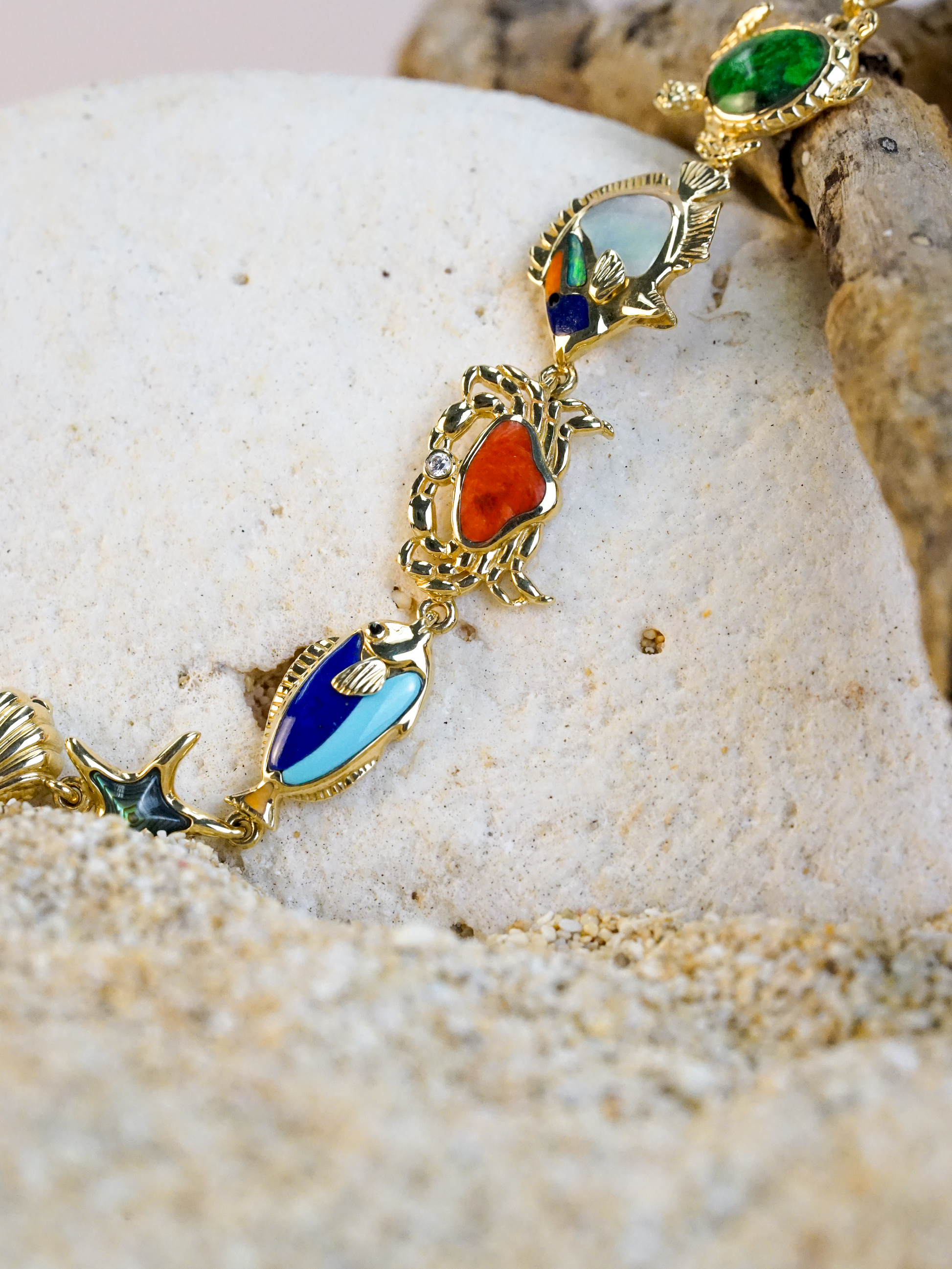 Gold bracelet with colorful reef creatures with gemstones on a sandy and white rock surface. Item No. 41943