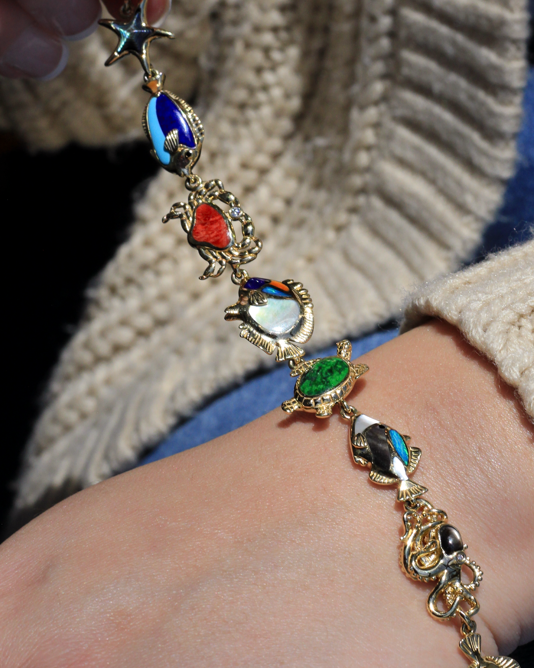 Gold and colorful reef life bracelet on a wrist with a textured background. Item No. 41943