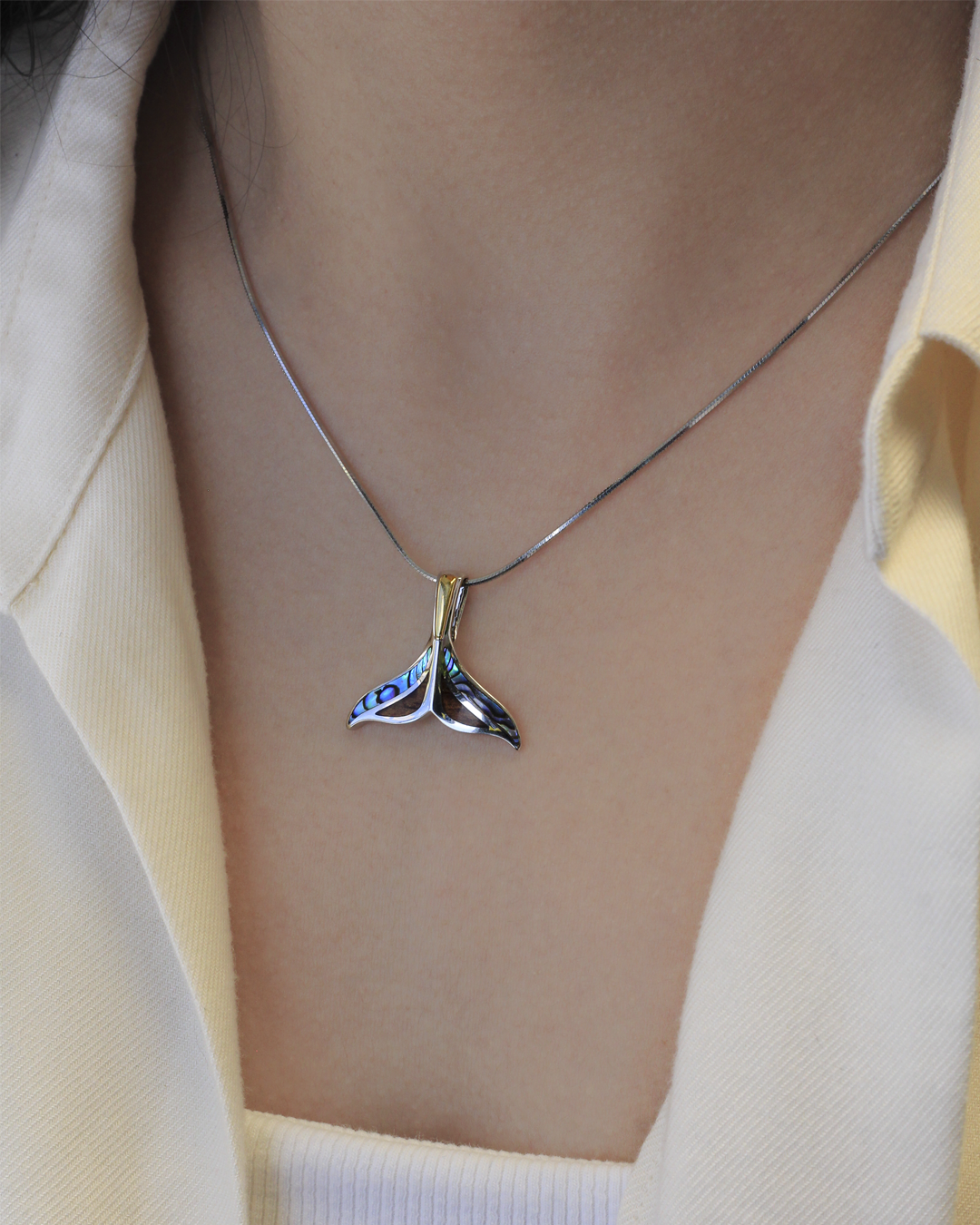 Close up of model wearing a silver whale tail necklace with gold accents and blue abalone shella nd brown Koa wood inlay. Item 45013