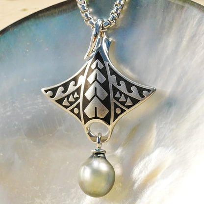 A silver chain with a stylized manta-ray pendant featuring black oxidized tattoo details and a dangling Tahitian teardrop pearl, shown close up against a glossy iridescent shell surface. Item No. 45069