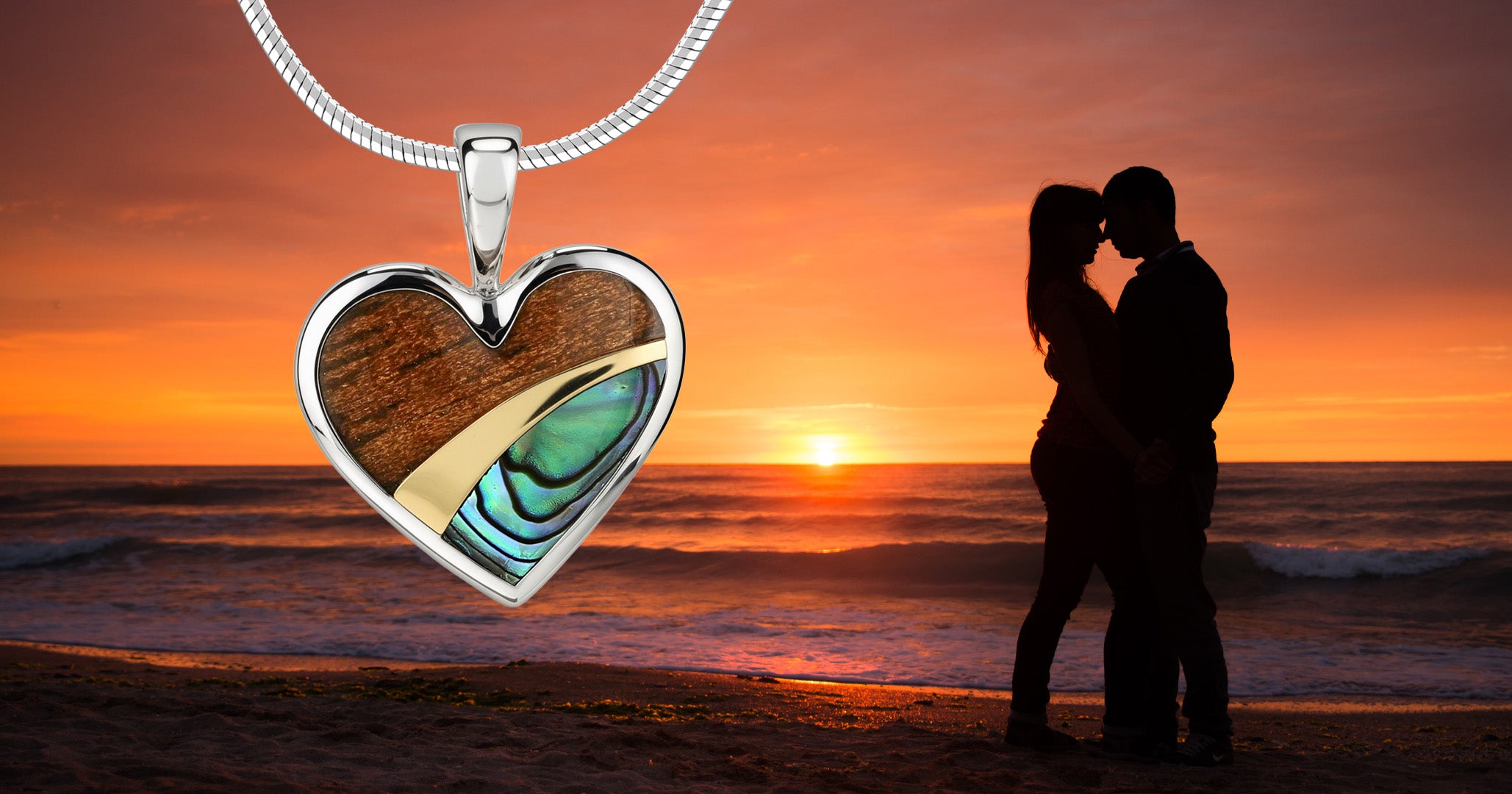 Silver heart-shaped pendant with  gold accent, Koa wood and abalone against a sunset beach background