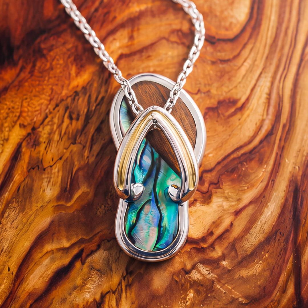 A silver slipper pendant with gold accent,  iridescent abalone shell and Koa wood inlay, displayed on a textured wooden background. Item No. 45404
