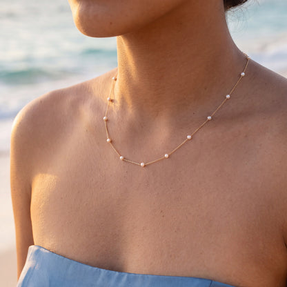 Close up pf a model wearing a yellow gold necklace with small, stationary white pearls. Item 773218